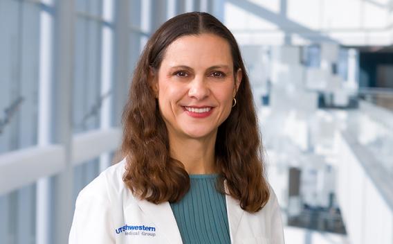 Smiling woman with long, dark, wavy hair, wearing a white UT Southwestern Medical Center lab coat.