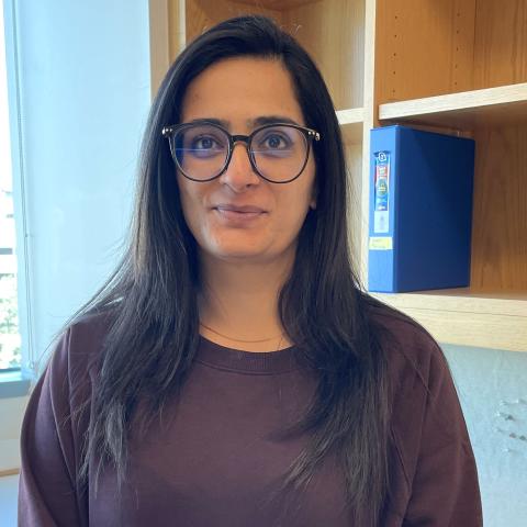 Woman with dark hair, round glasses, and dark sweatshirt stands in front of a lab desk