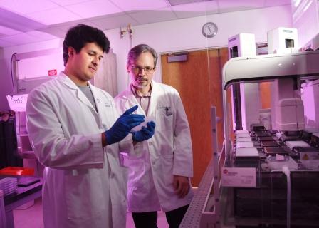 HTS Core scientist Irvin Garza and Core Director Bruce Posner inspect an assay plate as the Biomek FX delivers compounds for a large chemical screen.