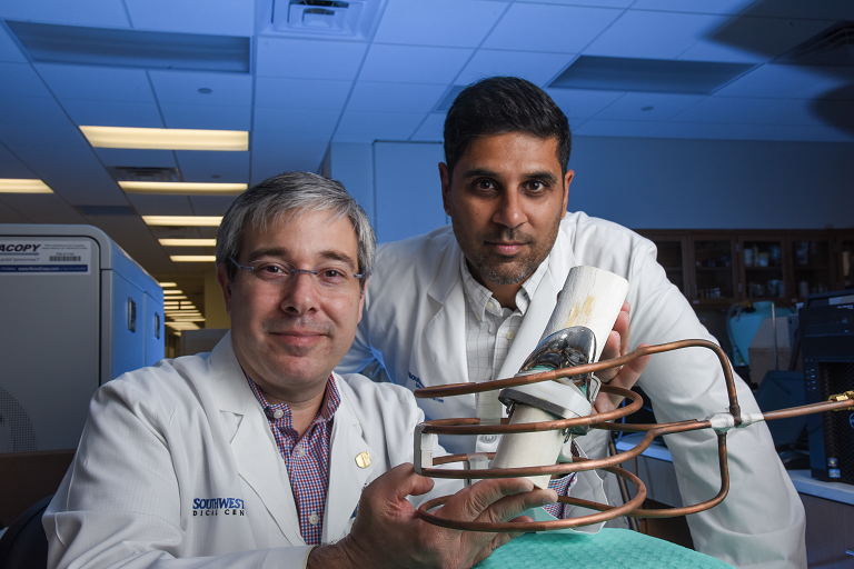 Two scientists wearing white lab coats in a lab, holding a device.