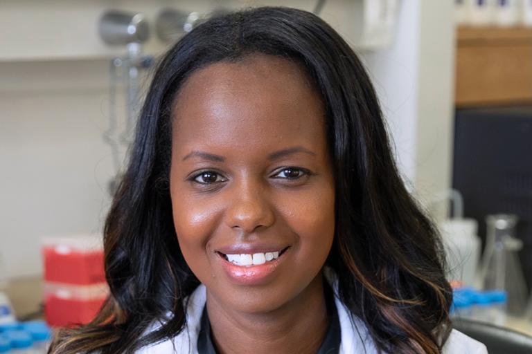 Dr. Josephine Thinwa, M.D. Ph.D. wearing a white lab coat, standing in a laboratory