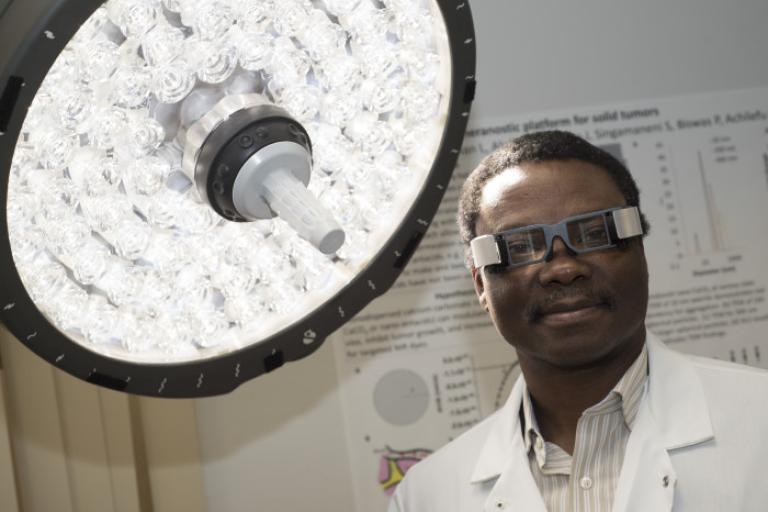 Dr. Achilefu in operating theater with bright light and googles.