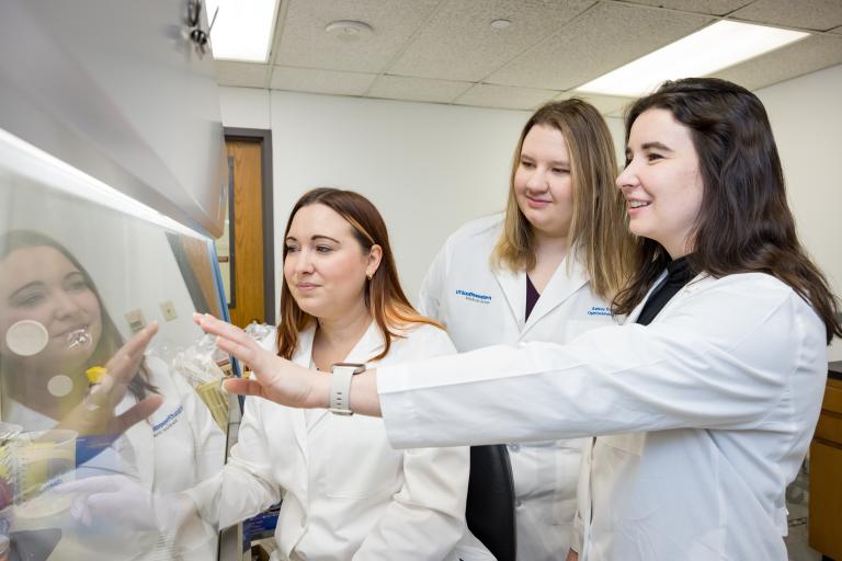Dr. Wert, Ashley Rowe, and Emily Nettesheim looking at lab materials under the hood.