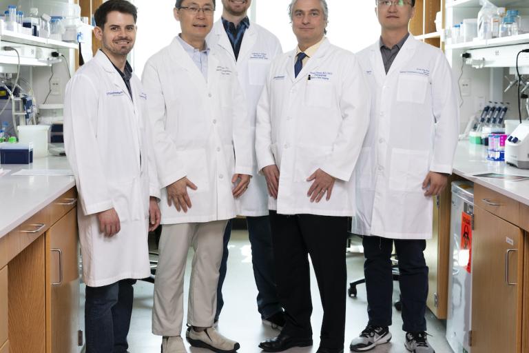 Five men wearing white UT Southwestern lab coats in a lab.