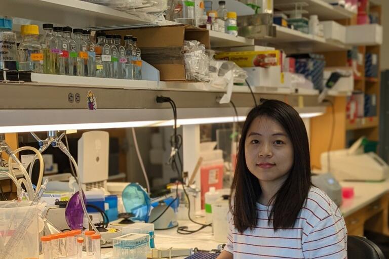 A woman with white shirt with horizontal stripes sitting at a lab bench