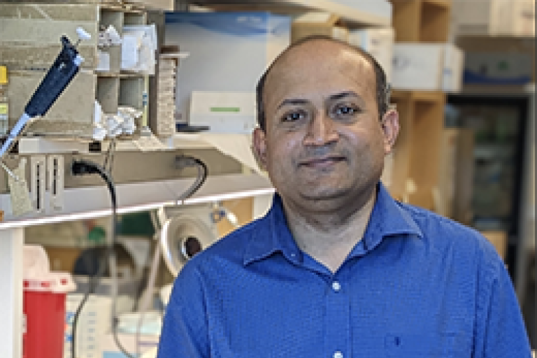 A man (Amitabh Ranjan) with a blue shirt stands at a lab bench