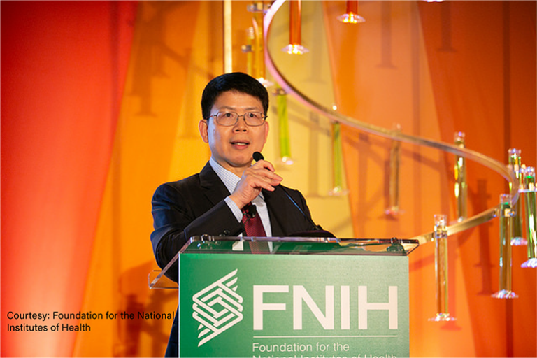 Man with dark hair and glasses speaking from a podium with the FNIH logo.