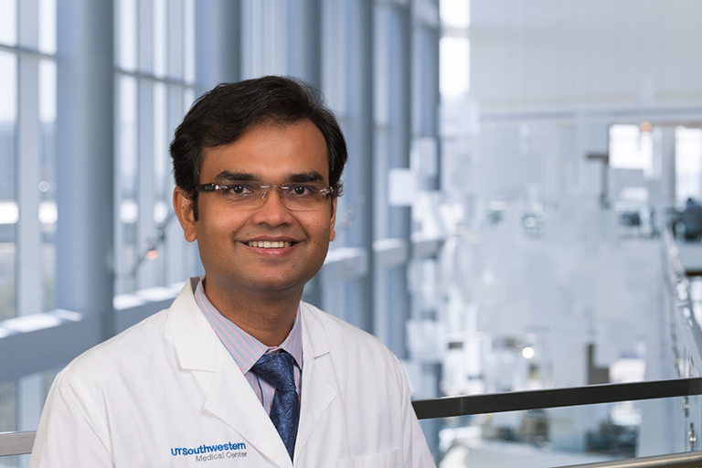 Dr. Ambarish Pandey wearing glasses, a white lab coat and striped shirt standing in the Clements University Hospital lobby