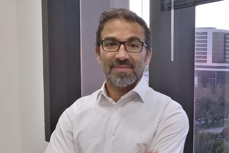 Dr. Hani Suleiman, wearing glasses and a white shirt standing in front of a window