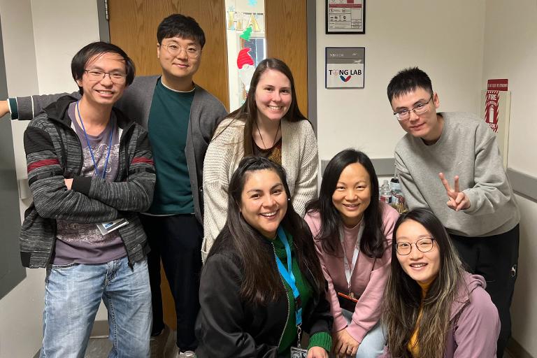 Dr. Dan Tong with five lab members gathered in front of the laboratory doorway.