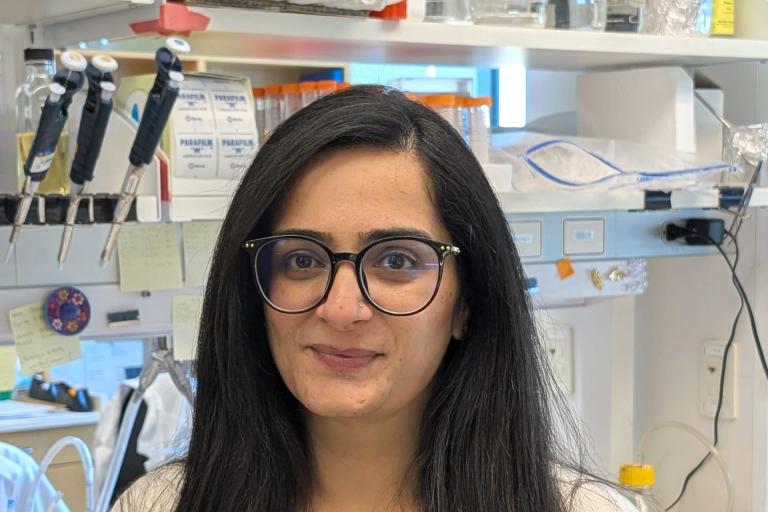 Woman with dark hair, round glasses, and dark sweatshirt stands in front of a lab desk
