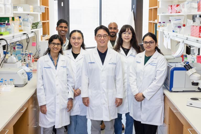 Dr. Park and his seven lab members wearing white coats and standing in his lab.