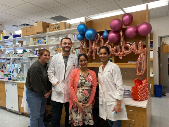 Alex, Arbi, Maggie, and Anju standing in front of balloons that say "Oh Baby"