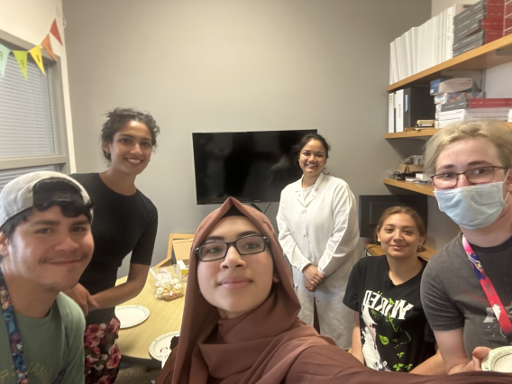 Abner, Anju, Zehra, Maggie, Alex, and Timea standing at a table where there is cake.