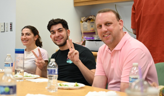 A woman and two men pose for the camera while sitting at a table
