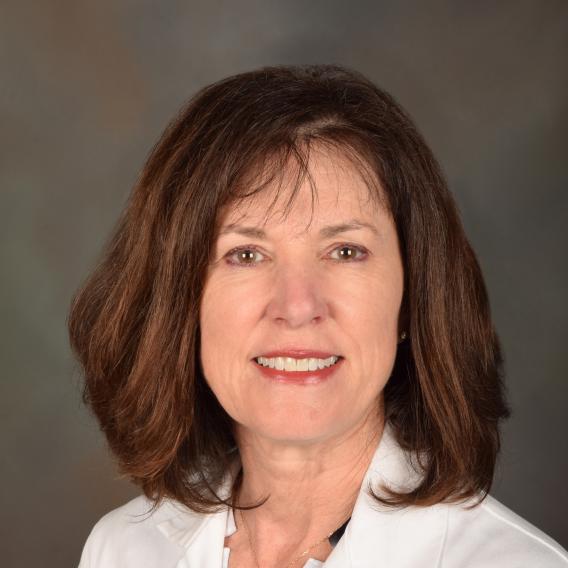 Smiling woman with auburn shoulder-length hair wearing a lab coat.