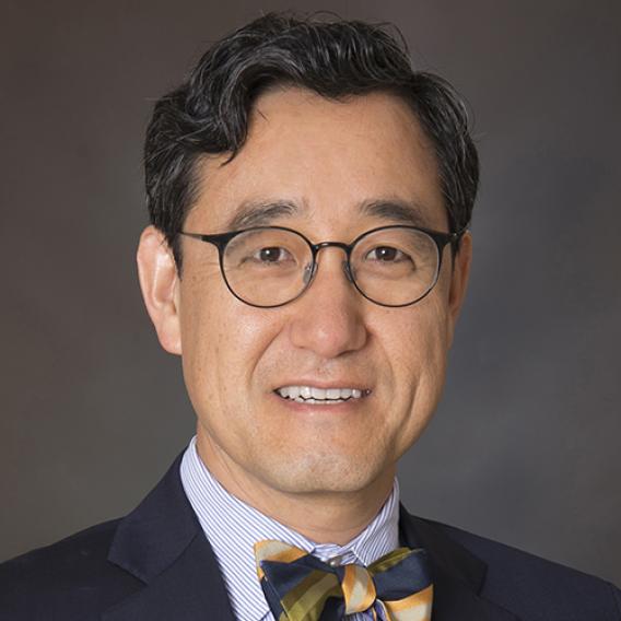 Dark-haired man with glasses wearing dark suit and bow tie.