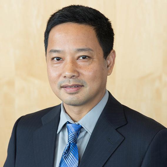 Man with black hair, wearing a dark suit, gray shirt, and blue plaid tie.