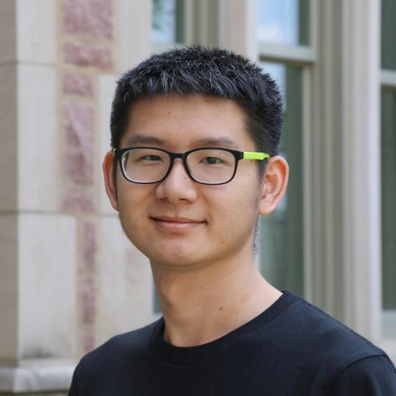 Shumeng Jiang wearing a black t-shirt and glasses standing in front of a building