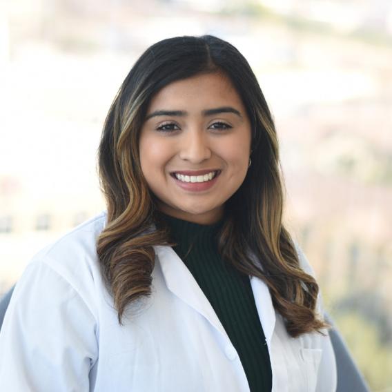Samantha Calvache a lab member wearing a lab coat and standing infront of a large window