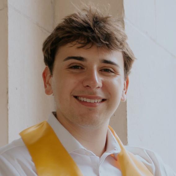 Michael Turner a lab member wearing a white and yellow shirt and standing infront of a brick wall