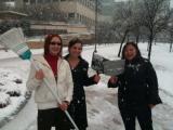 Three lab members outside in the snow, holding broom and dustpans