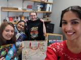 A selfie by Anju of her (right), Alex, Maggie, and T holding gifts and smiling. T is holding a shirt upside down.