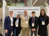 4 members of the greenberg lab with Dr. Greenberg (middle) standing infront of a poster presentation in a conference arena