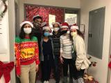 the lab group wearing holiday sweaters and standing in front of a holiday decorated door.