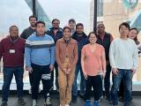 11 members of the Malladi Lab pose for the camera in front of windows
