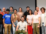 15 people pose for the camera in front of a wall
