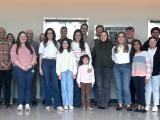 A group of 25 people stands in front of elevators all smiling. 