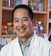 Smiling man with short dark hair, wearing a white lab coat.