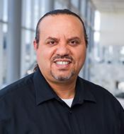 Smiling man with receding dark hair wearing a black shirt.