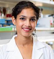 Smiling woman with dark hair, wearing a white lab coat.