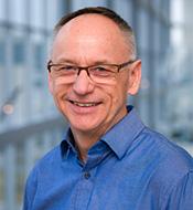Smiling man with graying hair and glasses, wearing a blue shirt.
