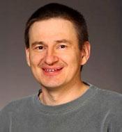 Smiling man with short brown hair, wearing a gray shirt.