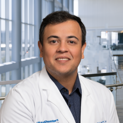 a man with short dark hair wearing a white lab coat standing in a hospital lobby