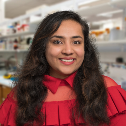 a woman with long dark hair wearing a red shirt standing in research laboratory.