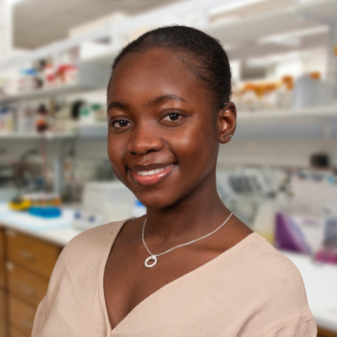 a woman with dark hair wearing a tan sweater stainding in a laboratory environment