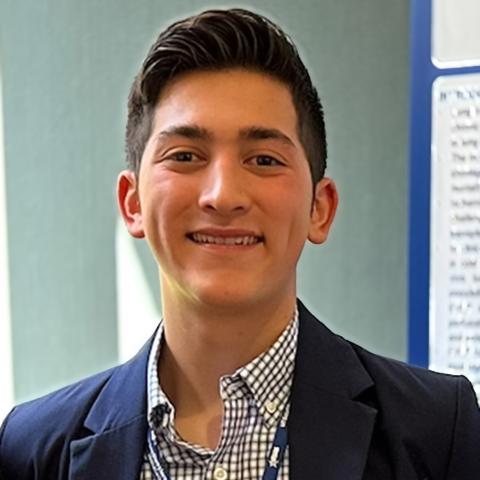 Smiling man with dark hair, wearing a plaid shirt and a suit jacket.