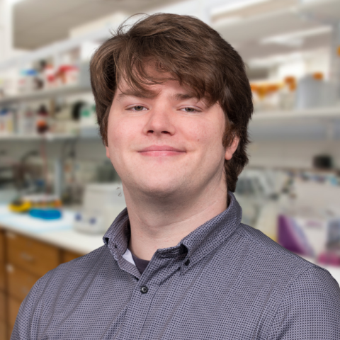 A man with short brown hair and a grey shirt standing in a laboratory