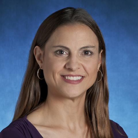 Smiling woman with long brown hair, wearing a purple top.