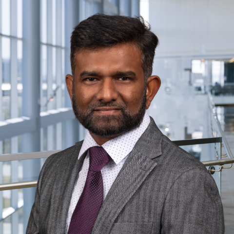 Nizam Ahamed wearing a grey suit and a maroon tie standing in the CUH lobby