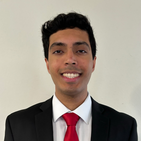 Abhinay Adlooru wearing a dark suit and a red tie standing in front of a blank wall