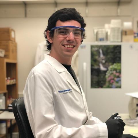 Alex Brennan in white lab coat and protective glasses in lab